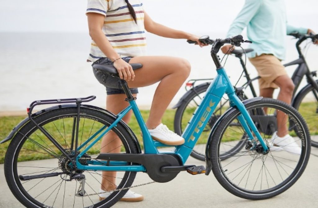 A woman standing near a blue bicycle from electric bike rental on a paved path. 