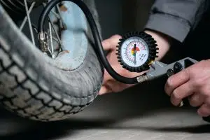 A worker is using a car tire inflating gun to inflate a motorbike wheel, as seen in the close-up.